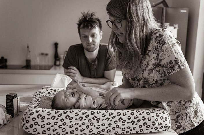 Newborn baby huilend op de verzorgingstafel met mama en papa.