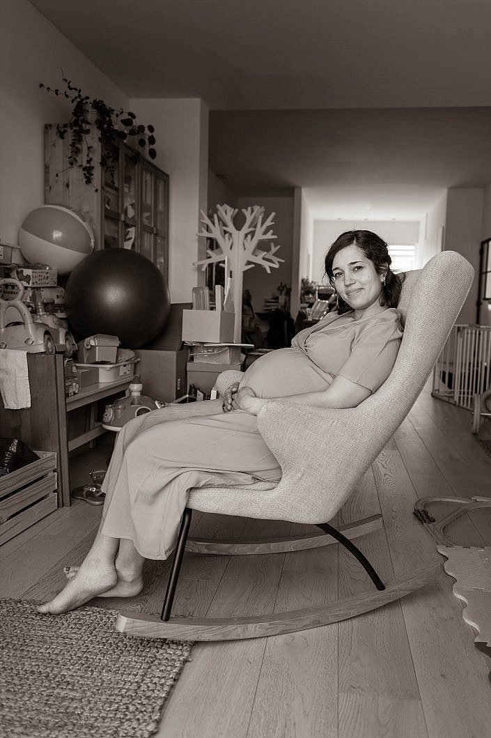 Zwangere vrouw in schommeltstoel kijkt recht in de lens.