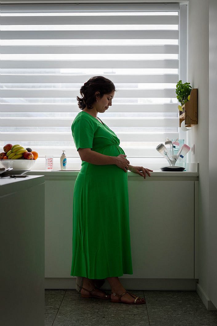 Zwangere vrouw met groen kleedje in de keuken voor het raam.