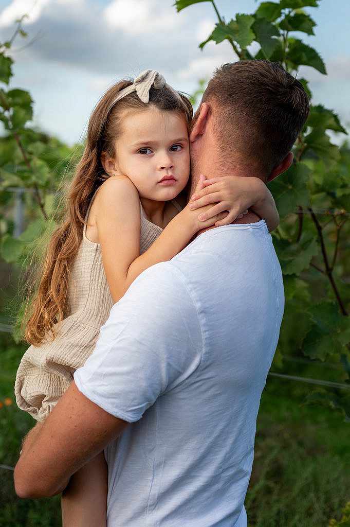 Foto shoot gezin van jong meisje bij papa op de arm kijkt recht in de lens.