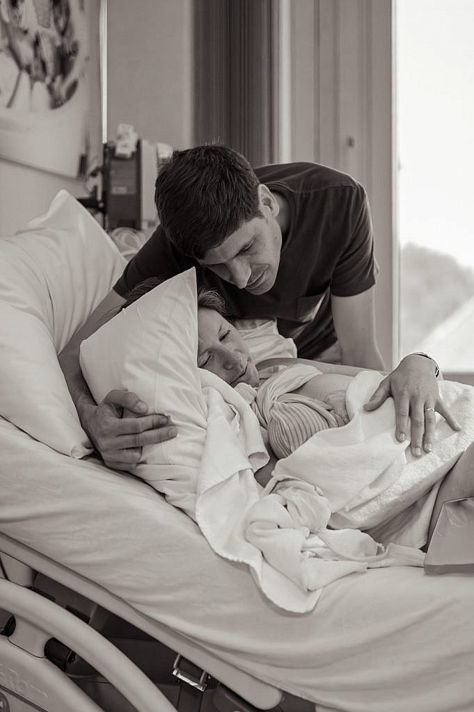 Papa houdt mama en baby vast in ziekenhuisbed.