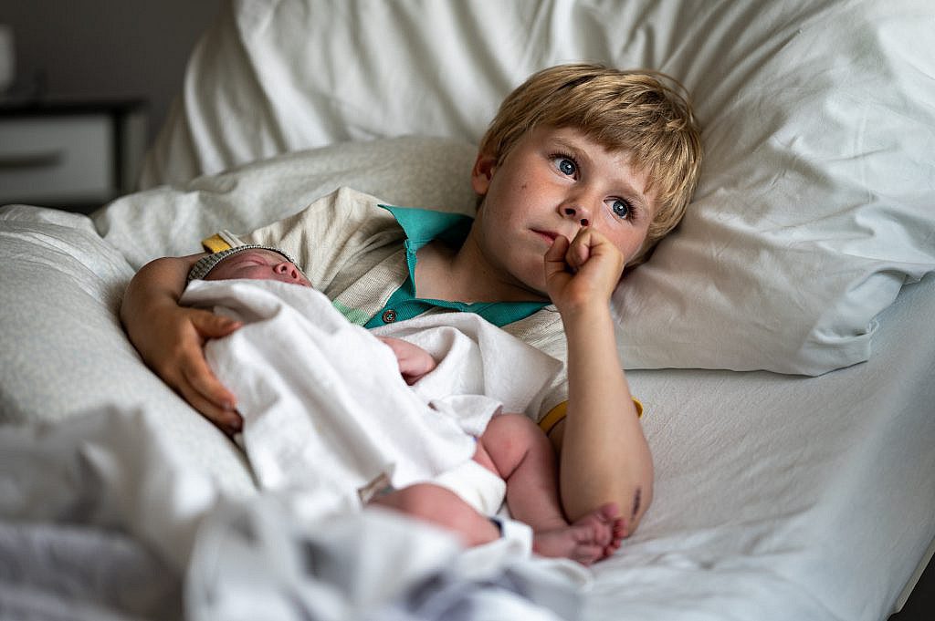 Pasgeboren baby in de armen van grote broer in ziekenhuisbed.