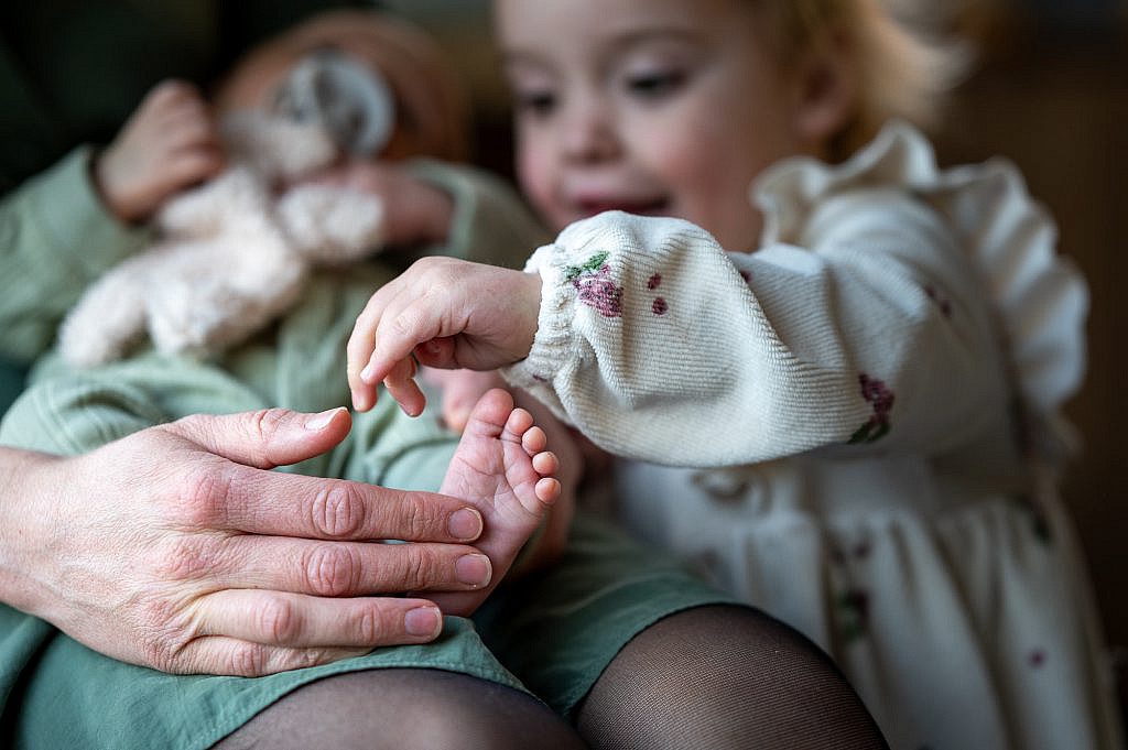 Newborn baby voetje met handjes van grote zus en mama.