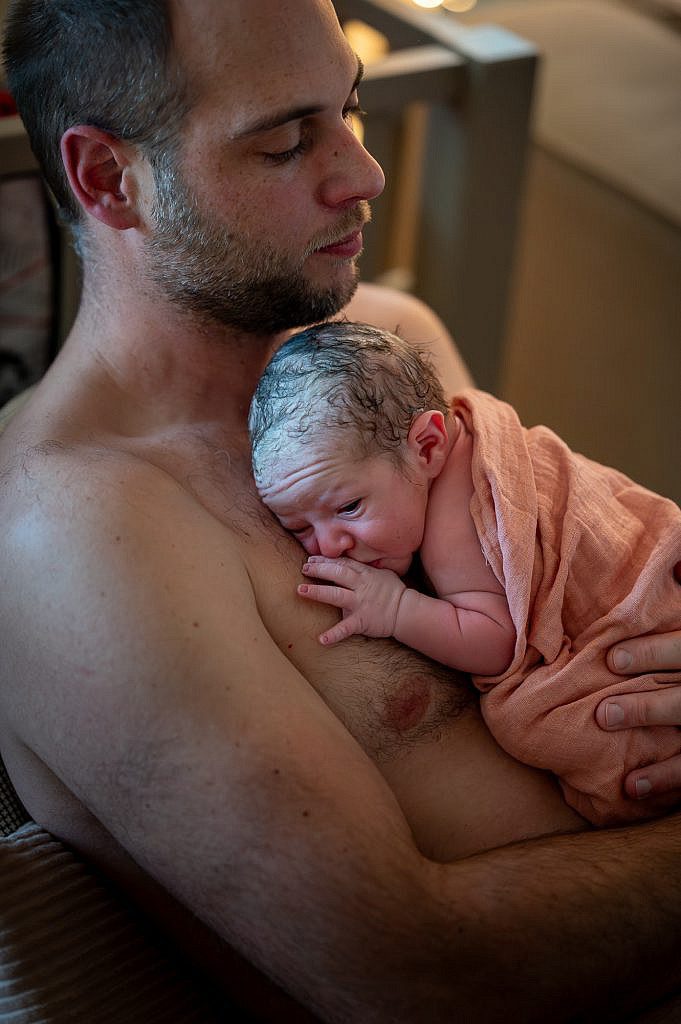 Newborn baby op de borst bij papa met oogjes open.