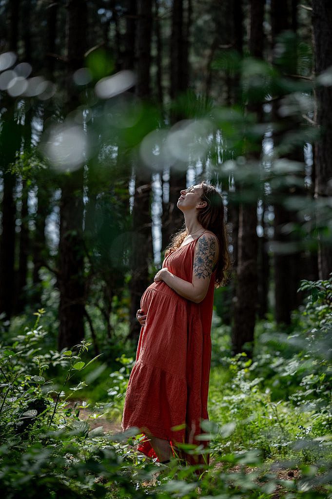Zwangere mama met handen op de buik in het bos.