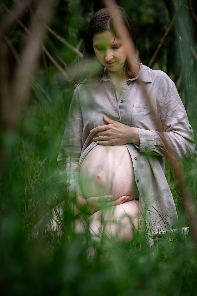 Zwangere vrouw zit geknield in het gras.