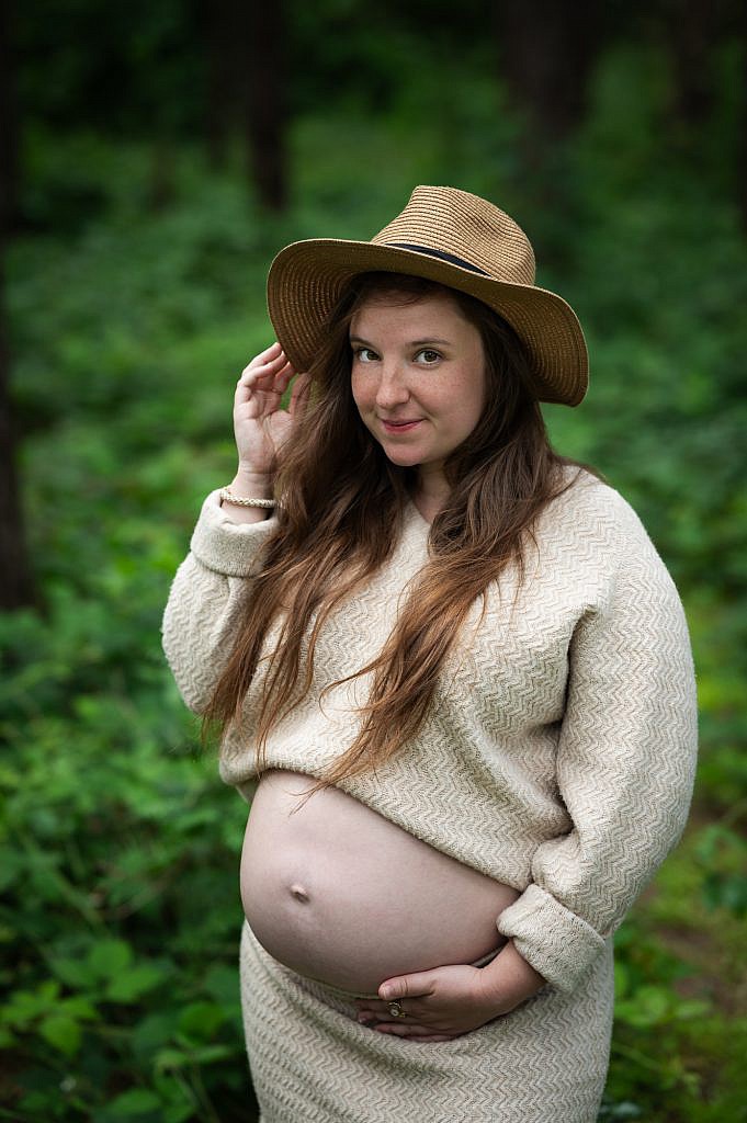 Zwangere vrouw houdt hoedje vast in het bos.