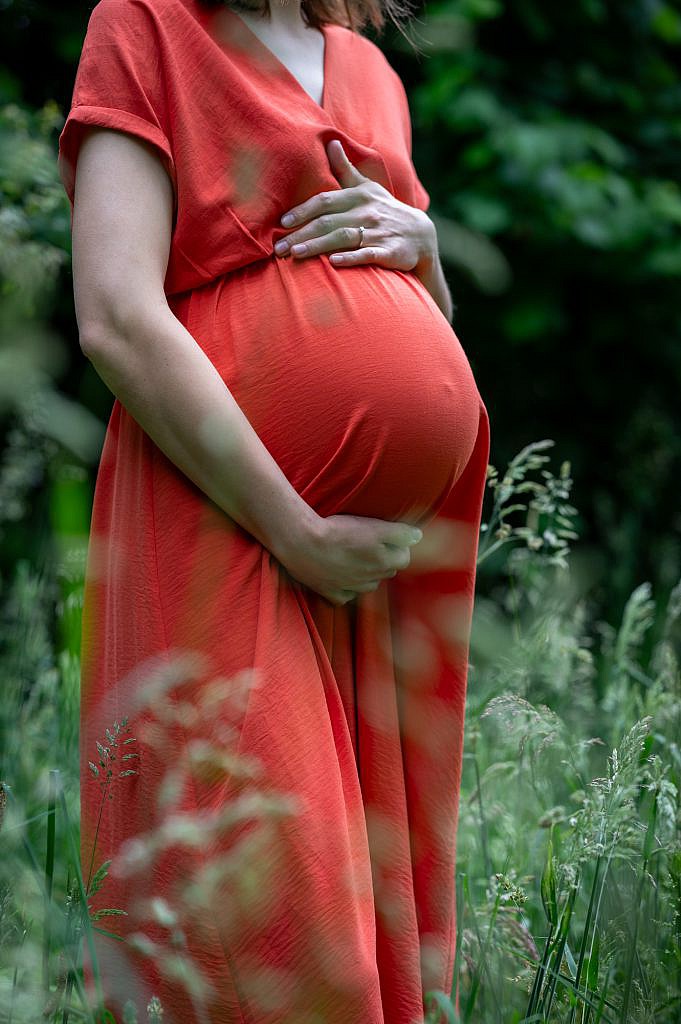 Zwangere vrouw houdt met beide handen haar buik vast.