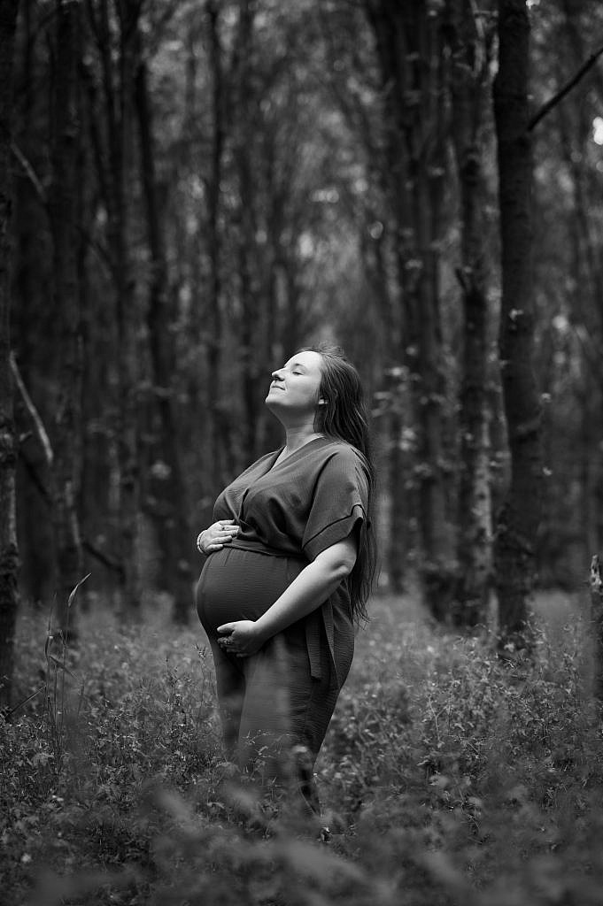 Zwart wit foto van zwangere vrouw met gesloten ogen in het bos