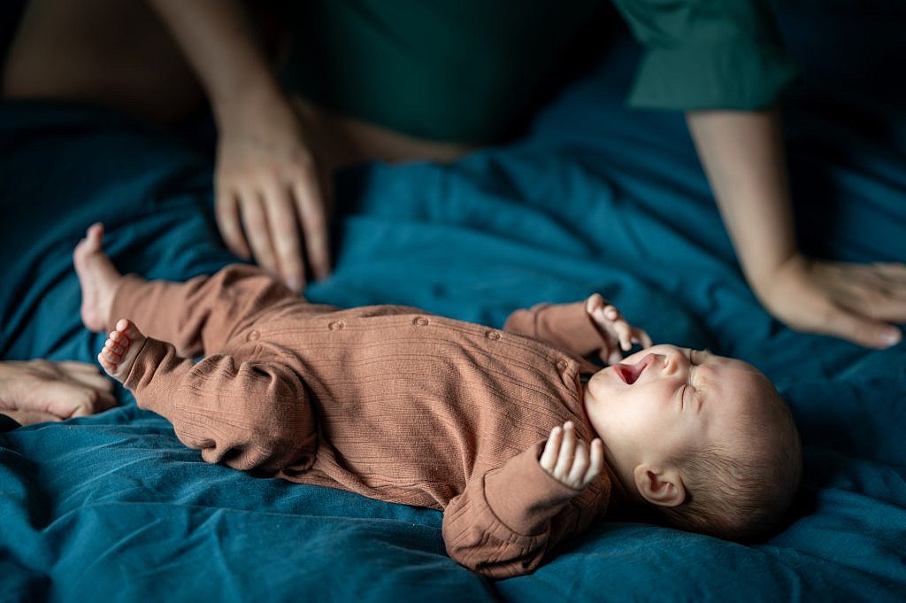 Newborn fotoshoot van geeuwende baby op bed.