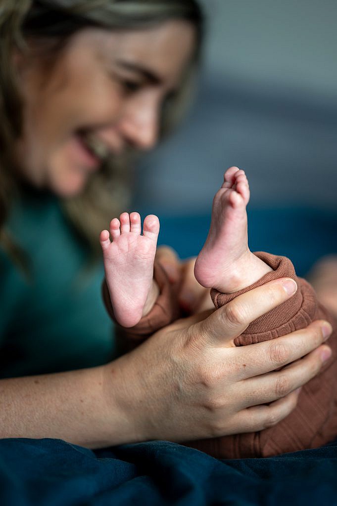 Newborn fotoshoot van baby voetjes met lachende mama op bed.