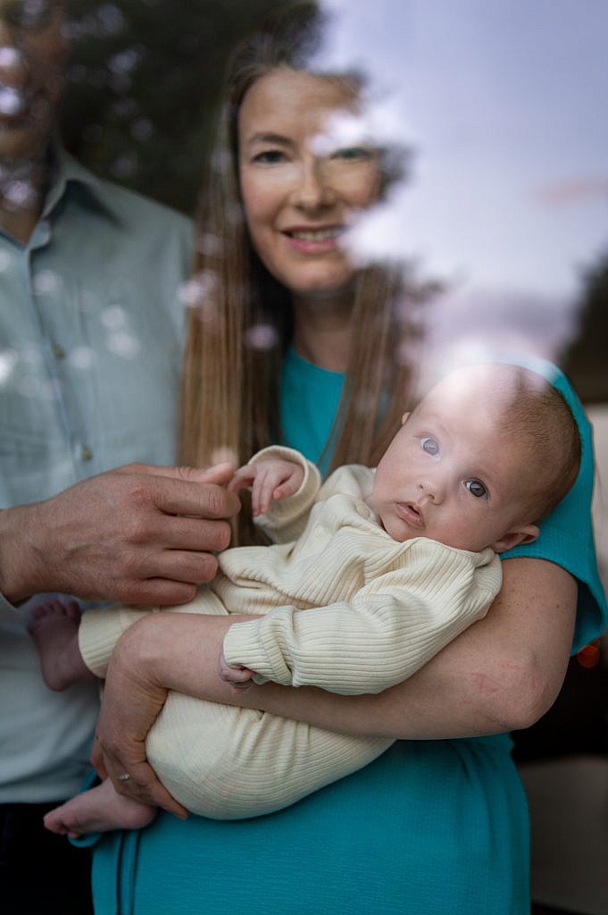 Newbornfotoshoot van baby in de armen van mama door een raam.