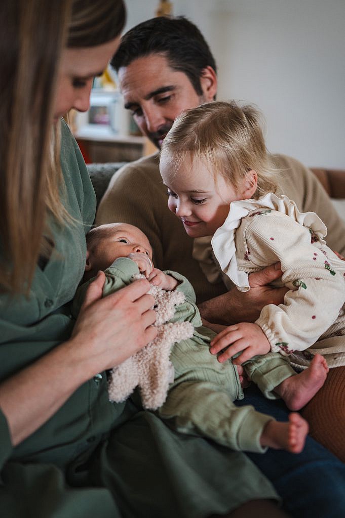 Newborn fotoshoot van baby met zusje die naar haar kijkt samen in de zetel.