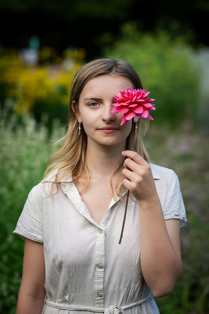 Jong meisje met roze dahlia voor een oog.