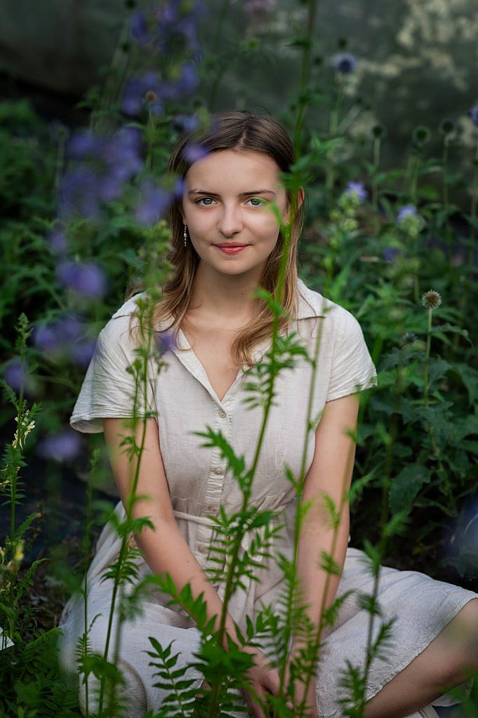 Jong meisje met groene ogen zit tussen paarse bloemen.