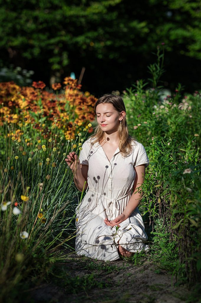 Jong meisje zit met gesloten ogen tussen de bloemen.