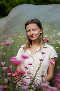 Jong meisje kijkt glimlachend vanachter roze bloemen.