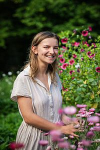 Jong meisje tussen roze bloemen kijkt lachend in de lens.