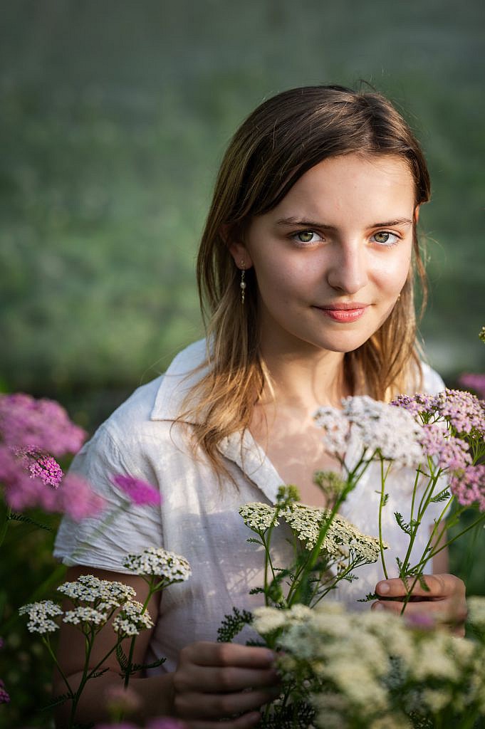 Jong meisje met groene ogen tussen roze bloemen.