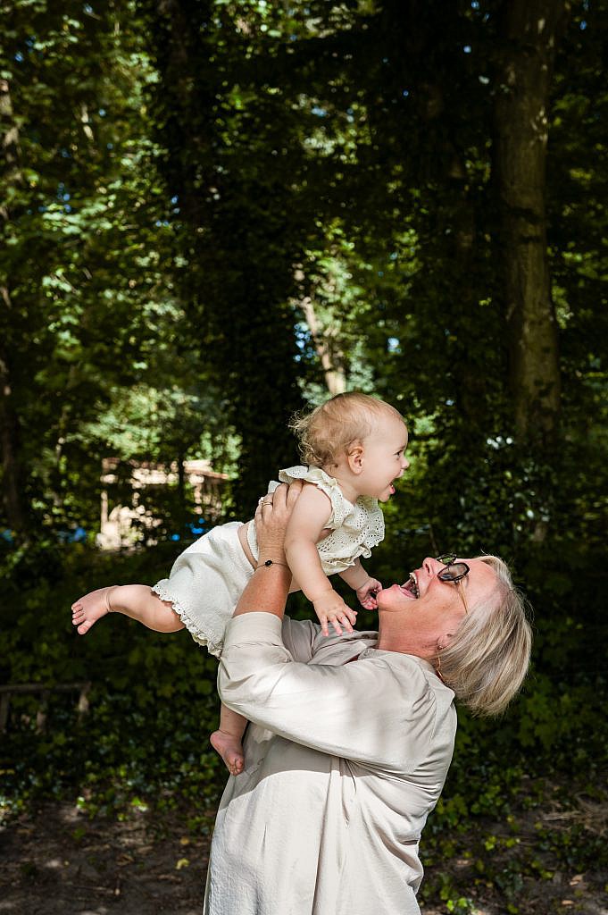 Oma houdt lachend haar baby kleindochtertje in de lucht op het bloemenveld.