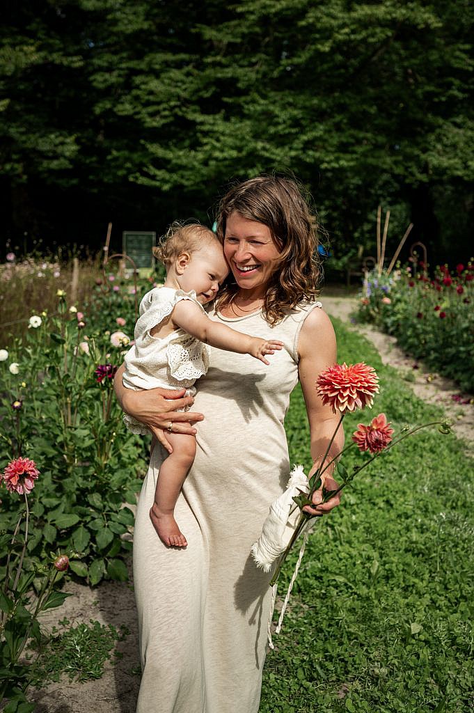 Mama met baby op de arm loopt lachtend in de bloemenplukweide.