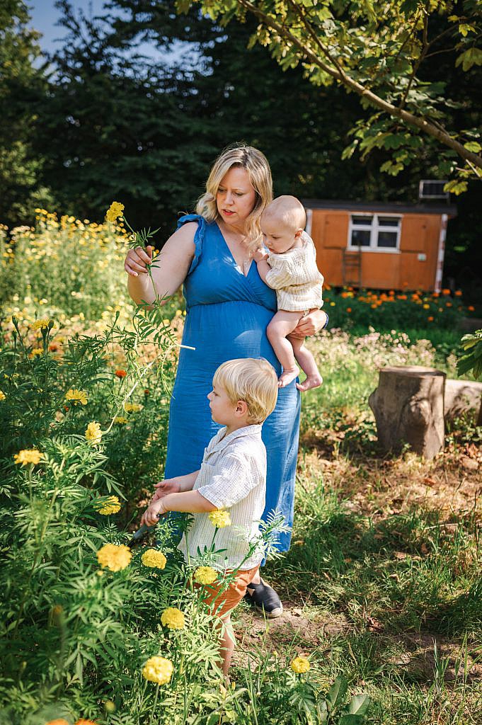 Mama met baby op de arm plukt bloemen in een bloemenveld.