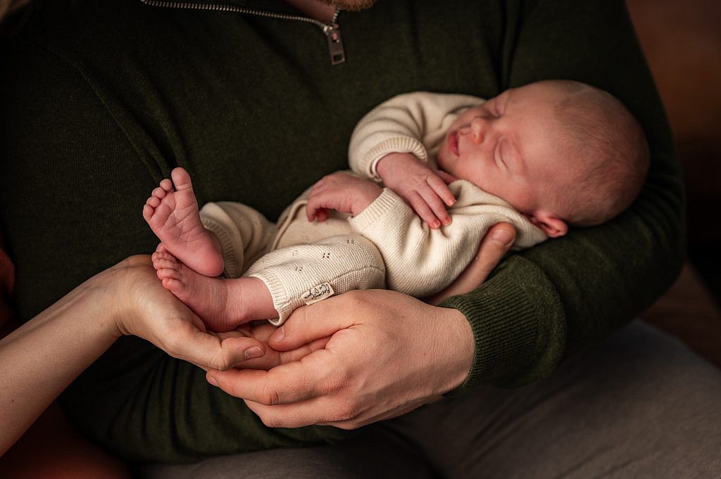 Slapende newborn baby ligt in de handen van mama en papa.