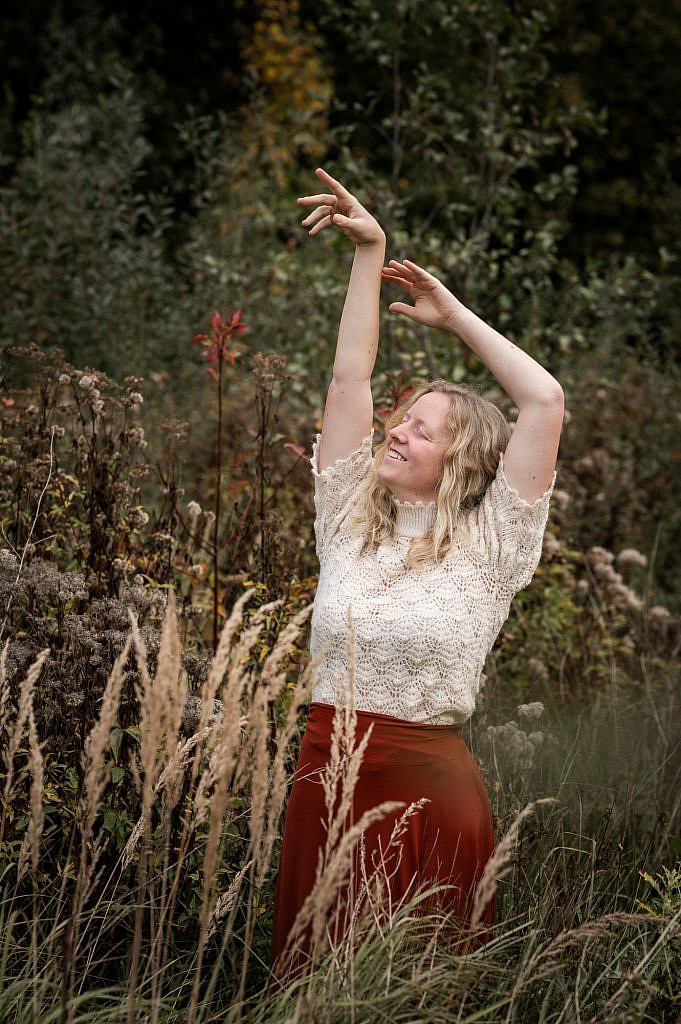 Jonge vrouw met gesloten ogen danst met de armen in de lucht in het hoge gras.