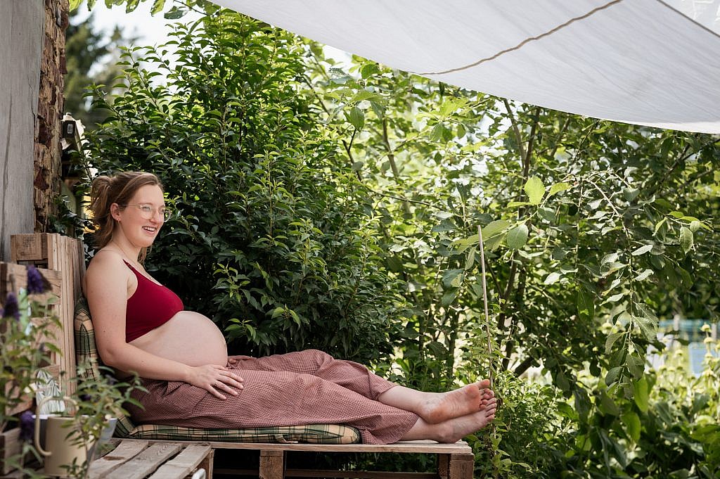 Zwangere vrouw zit met ontblote buik te genieten op een bankje in haar tuin, door de ogen van fotograaf Nele Martens uit Lievegem