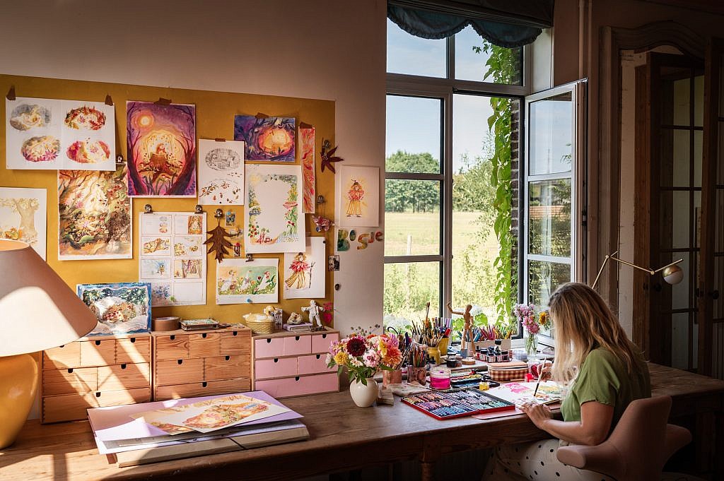 Illustrator van kinderboeken Suzan T'Hooft zittend aan haar bureau voor het raam gefotografeerd door Nele Martens fotograaf uit Lievegem.